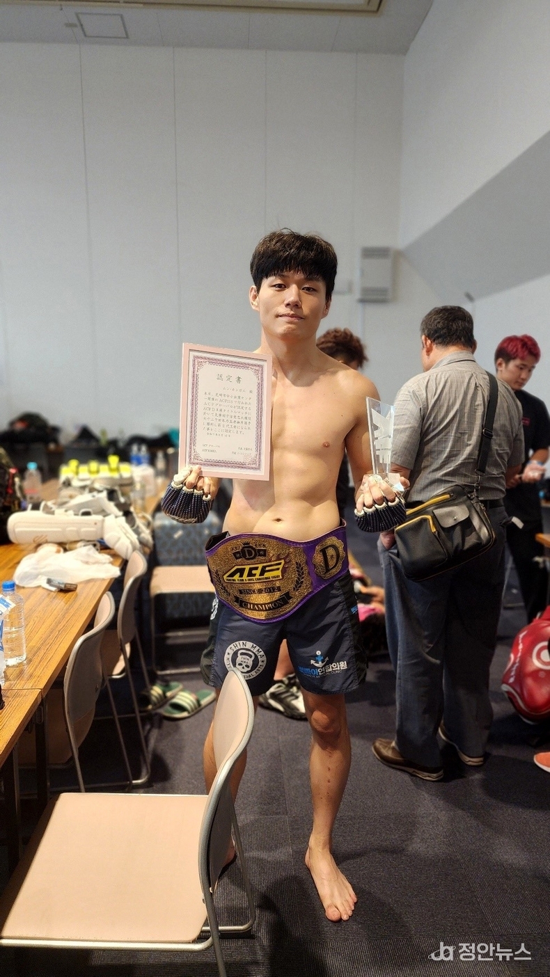 링에서 내려와서 챔피언벨트를 착용한 채로, 인증서와 트로피를 들고 기념사진을 찍는 중인 문홍범.